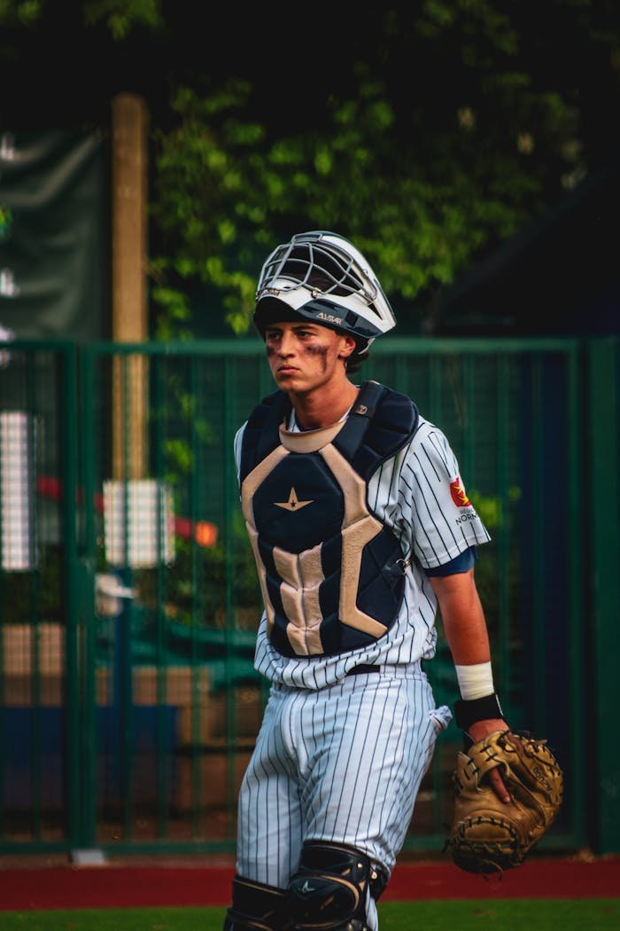 A young baseball catcher in protective gear walking on an outdoor field during the day.
